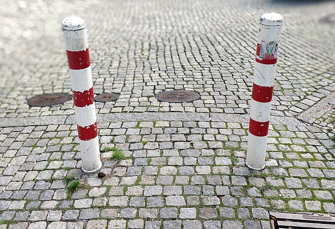 Zwei rotweisse Verkehrspoller zwischen Pflastersteinen