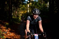 Gravelbikes liegen im Trend. Eine junge Frau mit Helm und schwazem Tricot fährt mit dem Gravelbike durch den Wald.