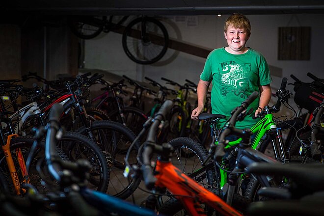 Ein Heranwachsender steht in einem Fahrradgeschäft zwischen vielen Velos.