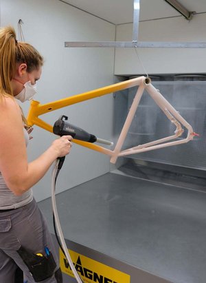 Eine Frau mit Schutzmaske pulverbeschichtet einen Fahrradrahmen.