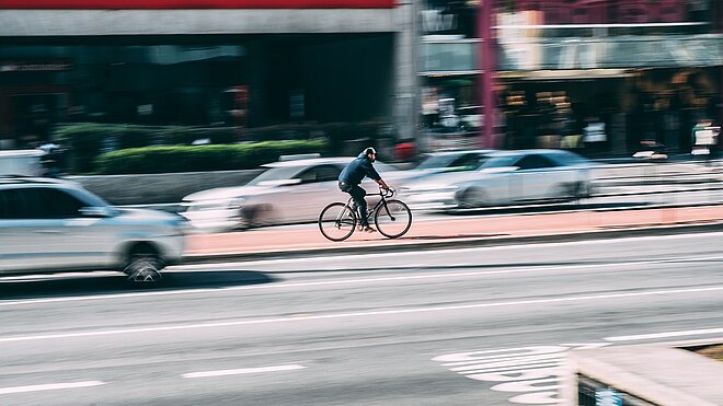 Ein Radfahrer fährt auf einem rot markierten Radweg in einer Stadt.