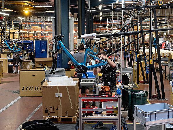 Ein Mann montiert in einer Fabrikhalle ein Fahrrad.