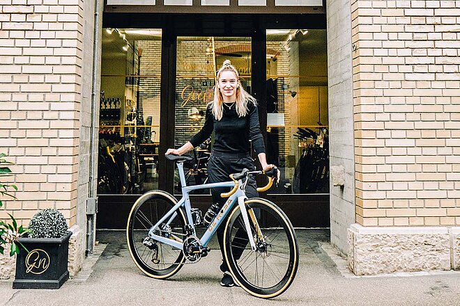 Velojournal stellt innovative Veloläden vor. Eine junge Frau mit blonden Haaren steht hinter einem Rennrad.