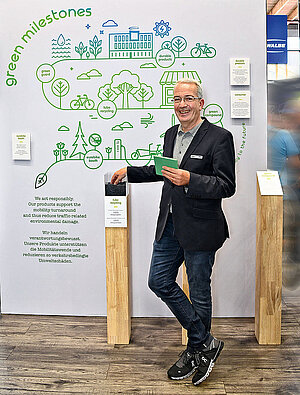 Ein Mann mit Sako und Turnschuhen steht vor einer Wand an der viele Zettel kleben