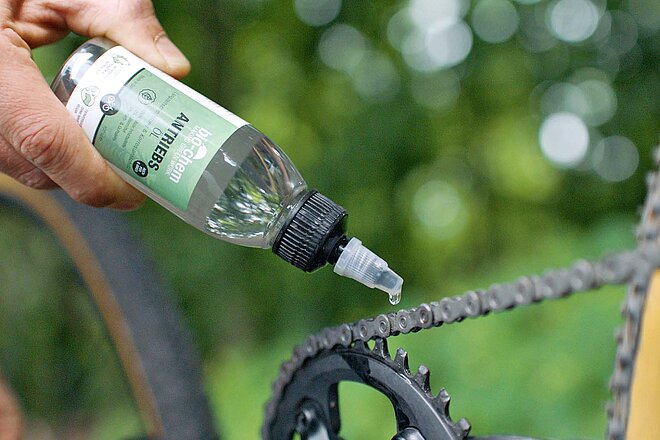 Fast alle Chemikalien belasten die Umwelt. Aus einer Flasche wird Öl auf eine Fahrradkette getropft.