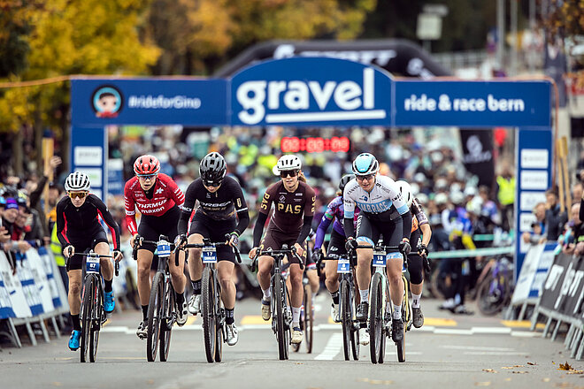 Radrennfahrerinnen starten bei einem Strassenrennen mit Gravelbikes.