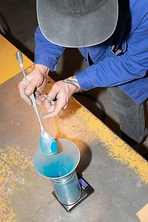 Eine Person füllt Farbe mit einem Löffel in einen Trichter.