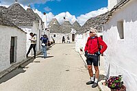 Ein Mann mit roter Jacke steht neben einer Reihe weiss getünchter Häuser. 