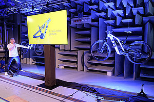 	Ein Mann mit Mikrophon spricht auf einer Bühne. Im Hintergrund hängen E-Mountainbikes.