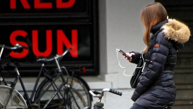 Frau sitz vor einem Plakat auf einem Fahrrad und schaut aufs Handy