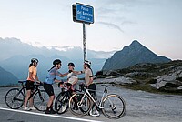 Frauen mit Rennrädern stehen unter dem Schild eines Alpenpasses.