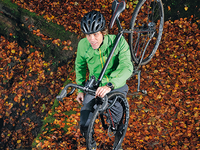Radfahrer mit grüner Jacke trägt Cyclocross-Bike auf der Schulter.