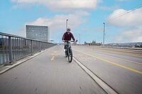 Potenzial schnelle E-Bikes. Ein Mann mit rotem Pullover und Helm fährt auf einem E-Bike über eine Brücke.
