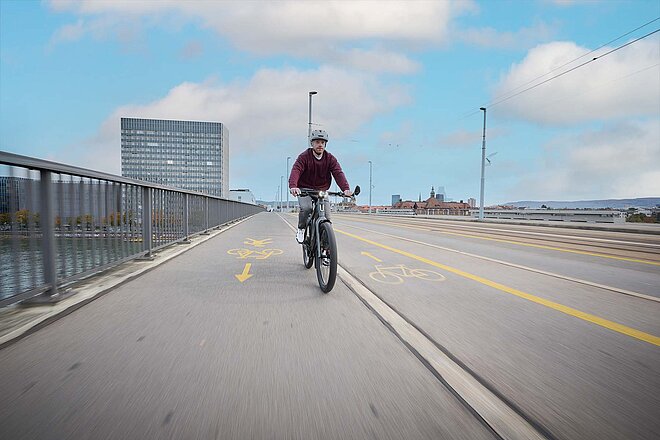Potenzial schnelle E-Bikes. Ein Mann mit rotem Pullover und Helm fährt auf einem E-Bike über eine Brücke.