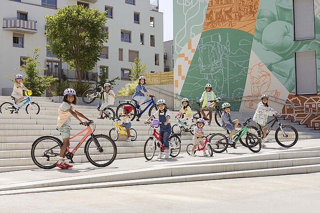 Kinder stehen mit Kinderfahrrädern auf einer grossen Treppe.