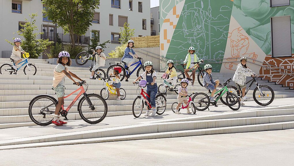 Kinder stehen mit Kinderfahrrädern auf einer grossen Treppe.