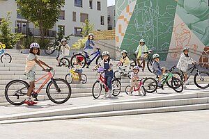 Kinder stehen mit Kinderfahrrädern auf einer grossen Treppe.