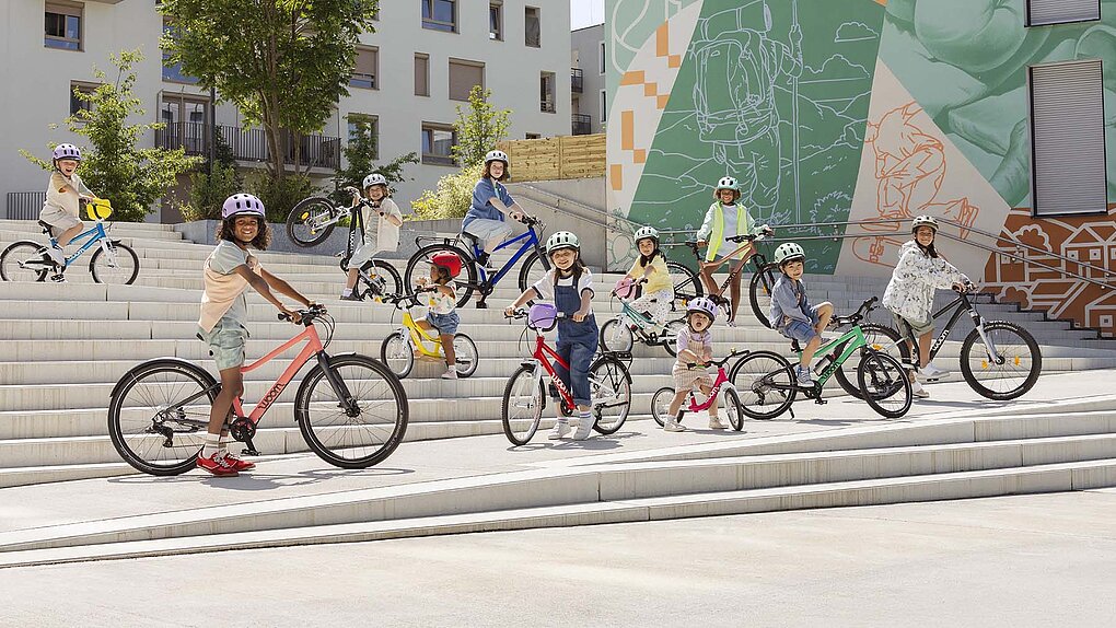 Kinder stehen mit Kinderfahrrädern auf einer grossen Treppe.