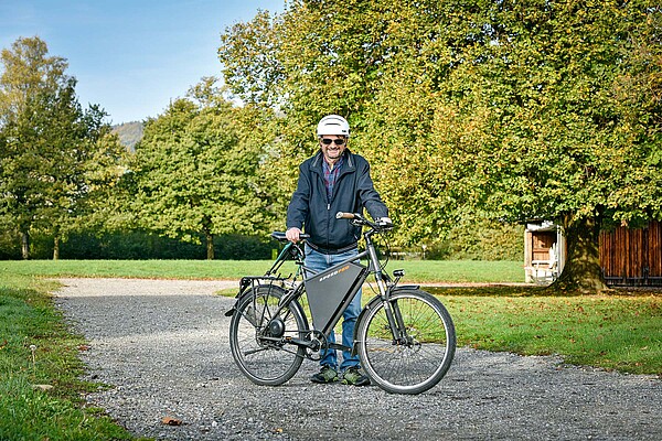 Ein Mann mit weissem Helm steht hinter einem Speedped E-Bike. Im Hintergrund ein Stadtpark.