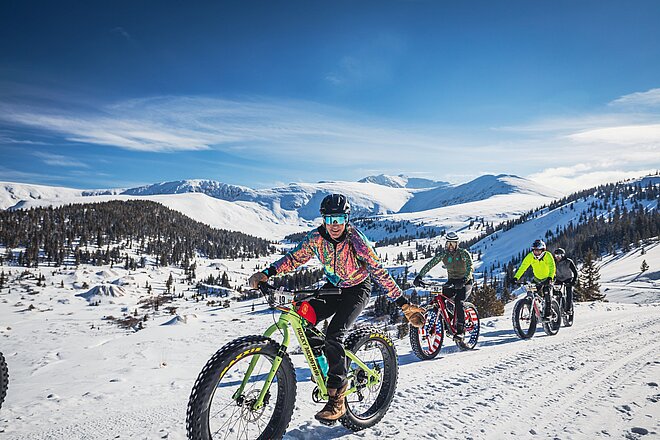Eine Gruppe von Velofahrern ist mit Fatbikes im Schnee unterwegs.