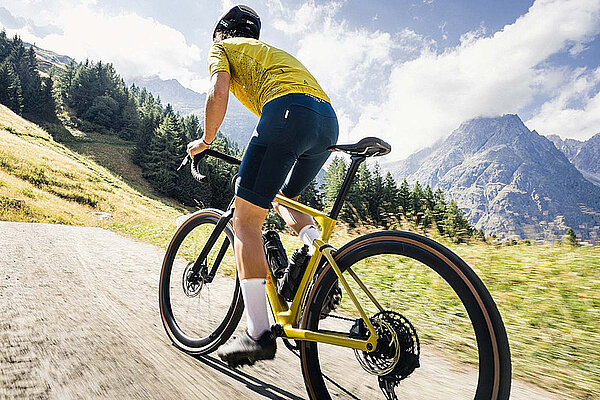 Eine Person mit gelbem Tricot fährt auf einem gelben Gravelbike auf einer Schotterstrasse.