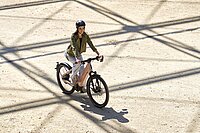 Eine Frau mit grüner Jacke fährt mit einem E-Bike über einen Platz.