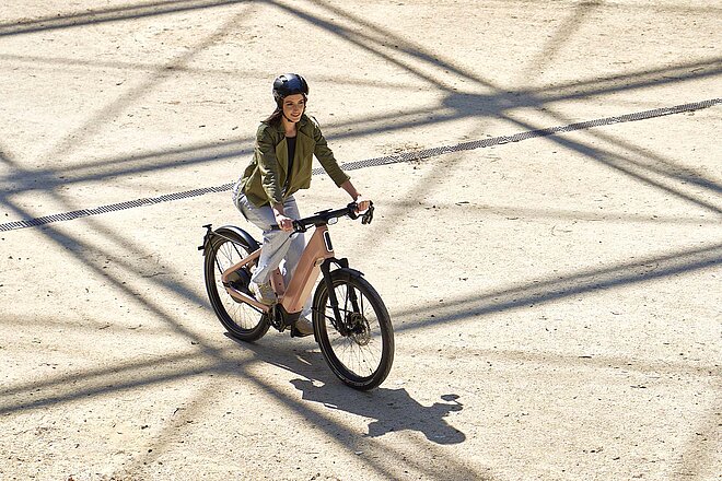 Eine Frau mit grüner Jacke fährt mit einem E-Bike über einen Platz.