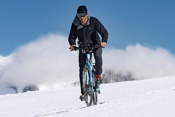 Tipps Tricks Radfahren im Winter. Ein Mann fährt mit dem Velo auf Schnee.