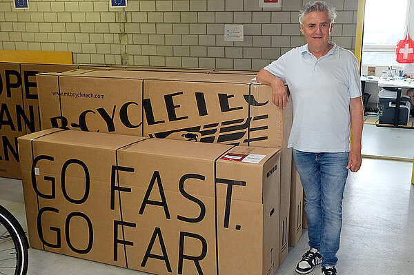 Opium Stromer Patenstreit. Ein Mann mit weissem Poloshirt und blauen Jeans steht neben Kartons in einem Lagerraum.