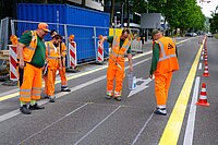 Bauarbeiter in oranger Arbeitskleidung bringen Markierungen auf einer Strasse an