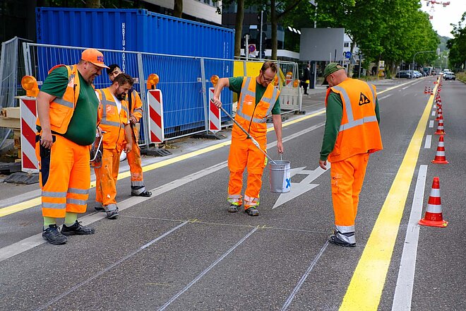 Bauarbeiter in oranger Arbeitskleidung bringen Markierungen auf einer Strasse an