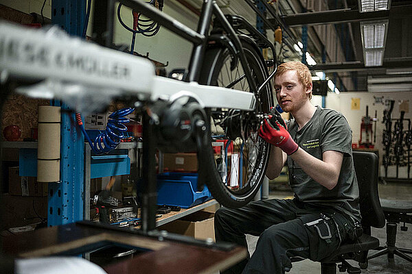 Ein Mann speicht das Rad eines Velos ein.