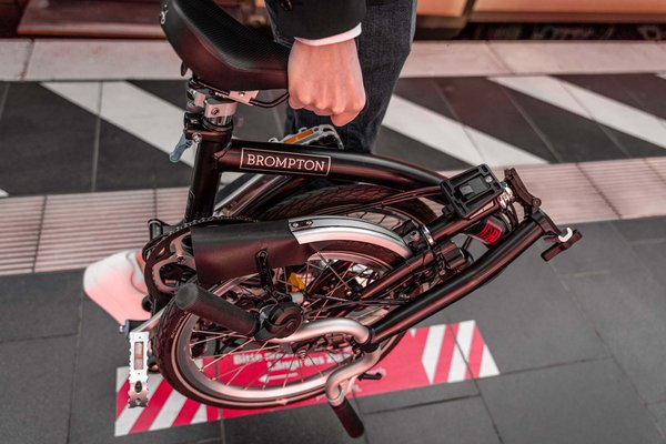 Die Deutsche Bahn und der Faltrad-Hersteller Brompton haben im Raum Stuttgart ein Pilotprojekt gestartet. Eine Person trägt ein gefaltetes Brompton Faltrad in der Hand.
