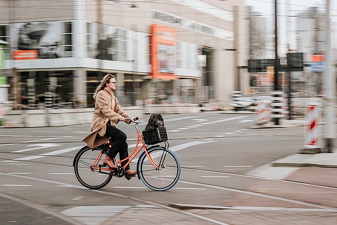 Eine Frau fährt auf einem organen Velo durch die Stadt.