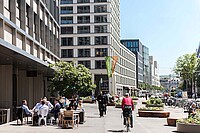 Eine Einkaufsstrasse mit modernen Gebäuden und Menschen die draussen in Cafés sitzen.