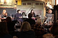 Vier Frauen sitzen auf einer Bühne und lesen aus einem Buch