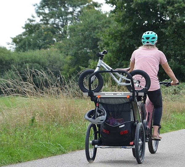 Frau fährt mit Veloanhänger am Waldrand entlang mit dem Laufrad im nika minirail 