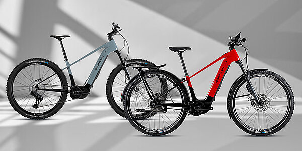 Zwei E-Bikes stehen vor einer grauen Wand.