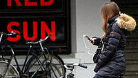 Frau sitz vor einem Plakat auf einem Fahrrad und schaut aufs Handy