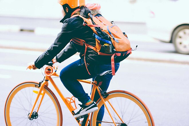 Frau mit organgem Helm und orangem Rucksack auf orange farbenem Velo