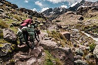 Bikepackerin schiebt vollbepacktes Fahrrad durch die Berge.