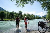 Radfahrer kühlen die Beine in einem Fluss ab.