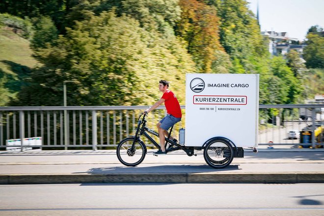 Vernehmlassung Cargobikes. Ein Mann im roten T-Shirt fährt auf einem Lastenrad.