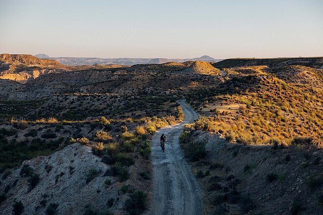 Ein Gravelbiker fährt auf einer Schotterstrasse.