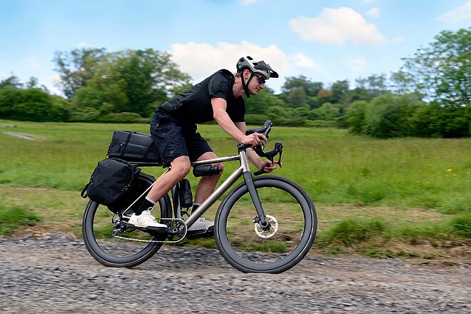 Ariel Dash Titan E-Gravelbike mit wenig Gewicht. Ein Mann mit kurzen Hosen und T-Shirt fährt auf deinem Gravelbike.