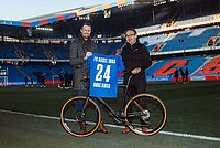 zwei männer stehen mit einem velo auf einem fussballfeld