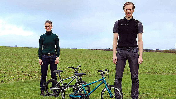 Kindervelo Marke Islabikes gibt auf. Ein Mann und eine Frau stehen neben Kindervelos auf einer Wiese.