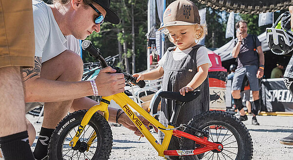 Testride Lenzerheide. Ein Kind steht neben einem gelben Laufrad.