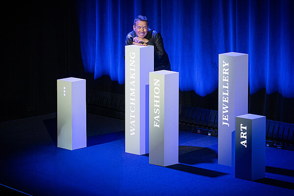 Ein Mann steht auf einer Bühne, die in blaues Licht getaucht ist.