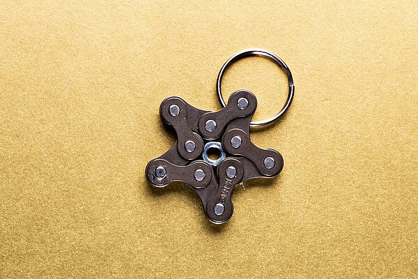 Sternförmiger Schlüsselanhänger aus Velokette auf goldenem Untergrund.